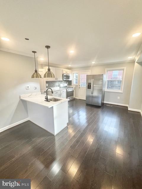 kitchen featuring white cabinetry, sink, hanging light fixtures, stainless steel appliances, and kitchen peninsula