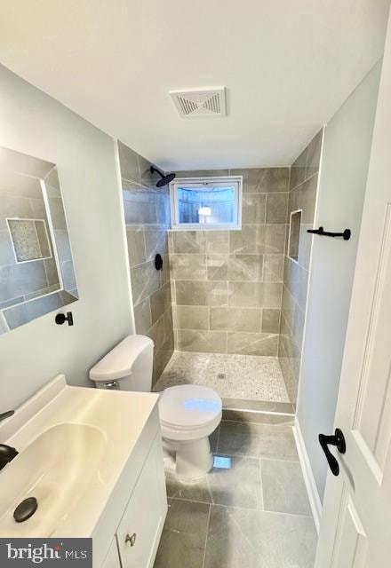 bathroom featuring tile patterned flooring, vanity, toilet, and tiled shower