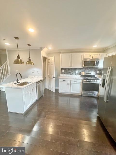 kitchen with sink, kitchen peninsula, decorative light fixtures, white cabinets, and appliances with stainless steel finishes