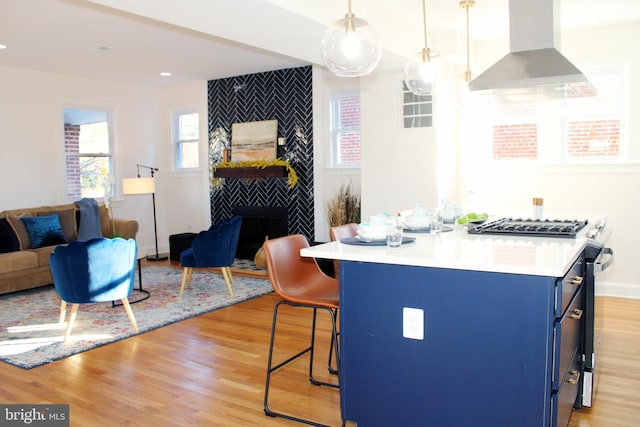 kitchen with hanging light fixtures, wall chimney range hood, blue cabinets, a breakfast bar area, and light wood-type flooring