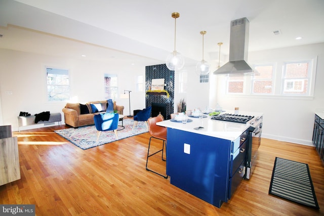 kitchen with gas range, a healthy amount of sunlight, hanging light fixtures, wall chimney range hood, and blue cabinets