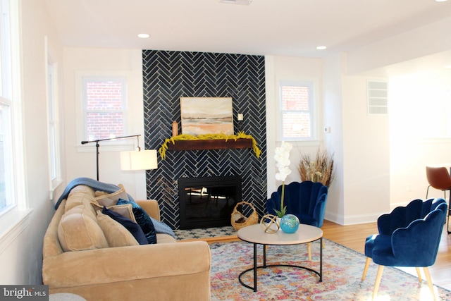 living room with a tiled fireplace, plenty of natural light, and light wood-type flooring