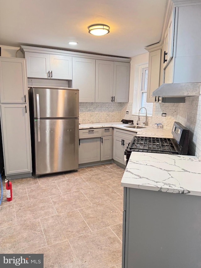 kitchen featuring gray cabinetry, backsplash, sink, appliances with stainless steel finishes, and light stone counters