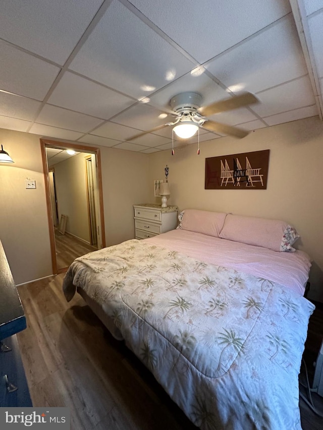 bedroom with ceiling fan, a drop ceiling, and wood-type flooring