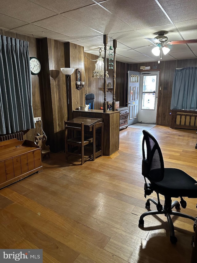 office space with a paneled ceiling, ceiling fan, wooden walls, and light hardwood / wood-style floors