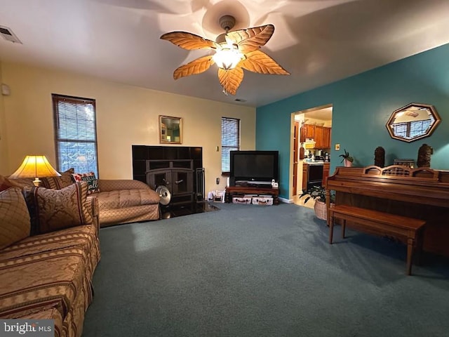 carpeted living room featuring a wood stove and ceiling fan