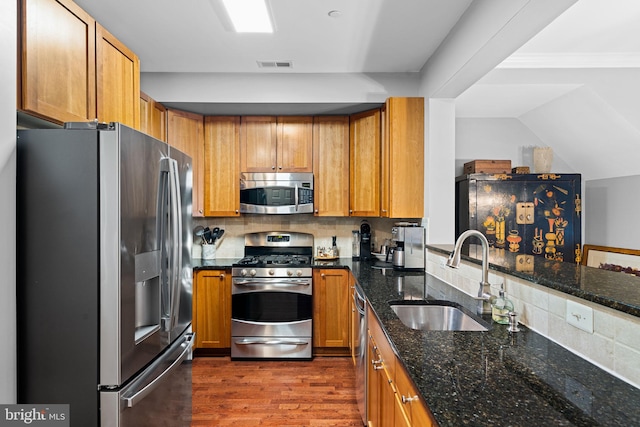 kitchen with sink, dark hardwood / wood-style floors, decorative backsplash, dark stone countertops, and appliances with stainless steel finishes