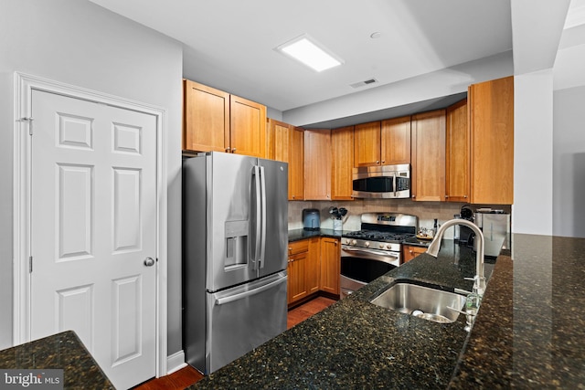 kitchen with backsplash, sink, appliances with stainless steel finishes, and dark stone counters