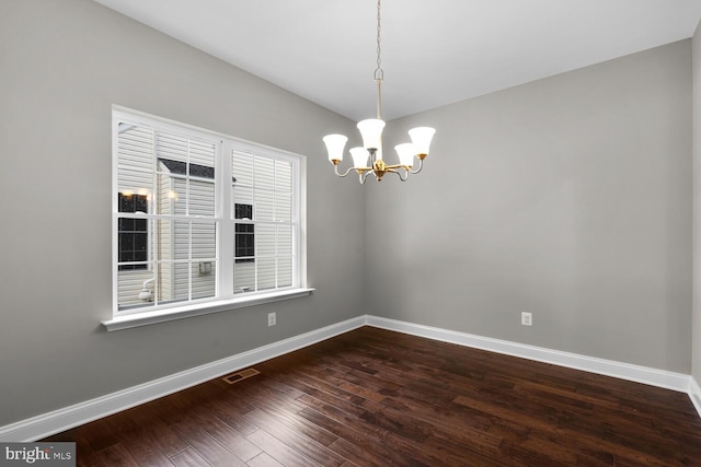 spare room featuring a chandelier and dark wood-type flooring