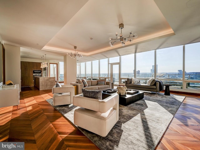 living room featuring light parquet flooring, an inviting chandelier, and a tray ceiling