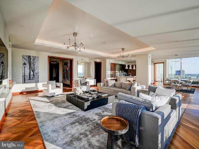 living room with a tray ceiling, parquet floors, a healthy amount of sunlight, and an inviting chandelier