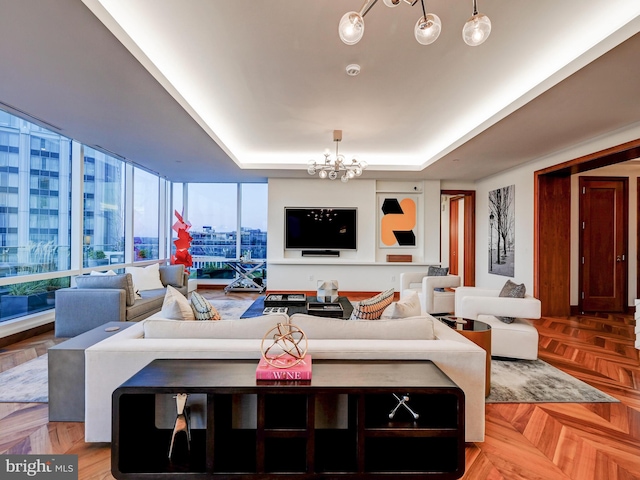 living room featuring light parquet floors, a tray ceiling, an inviting chandelier, and expansive windows