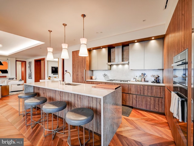 kitchen featuring wall chimney exhaust hood, a kitchen breakfast bar, sink, and decorative light fixtures