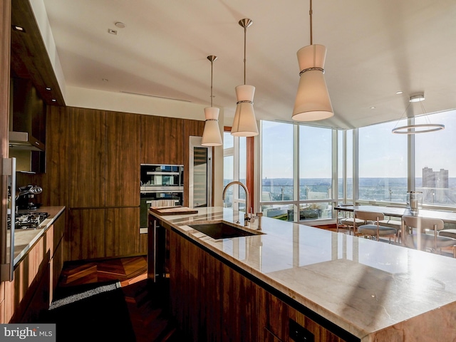 kitchen featuring wood walls, a center island with sink, sink, decorative light fixtures, and stainless steel appliances