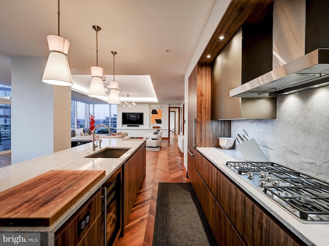 kitchen with decorative backsplash, wall chimney exhaust hood, stainless steel gas cooktop, sink, and a kitchen island