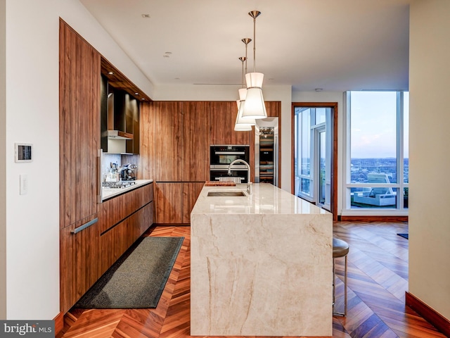 kitchen with sink, wall chimney range hood, an island with sink, pendant lighting, and a breakfast bar