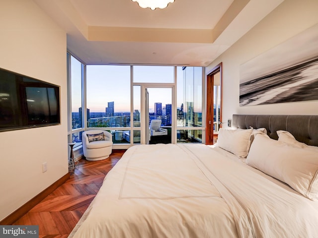 bedroom with dark parquet flooring, a raised ceiling, and a wall of windows