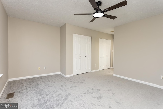 unfurnished bedroom with multiple closets, ceiling fan, light carpet, and a textured ceiling