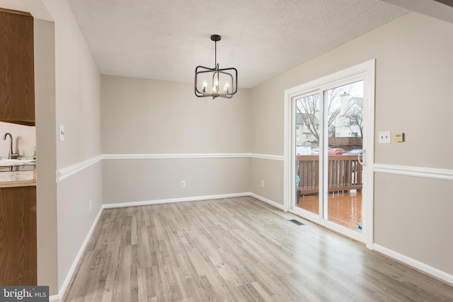 unfurnished dining area featuring sink, a chandelier, a textured ceiling, and light hardwood / wood-style floors