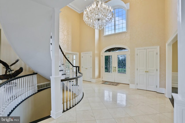 foyer featuring french doors, a towering ceiling, ornamental molding, light tile patterned floors, and an inviting chandelier