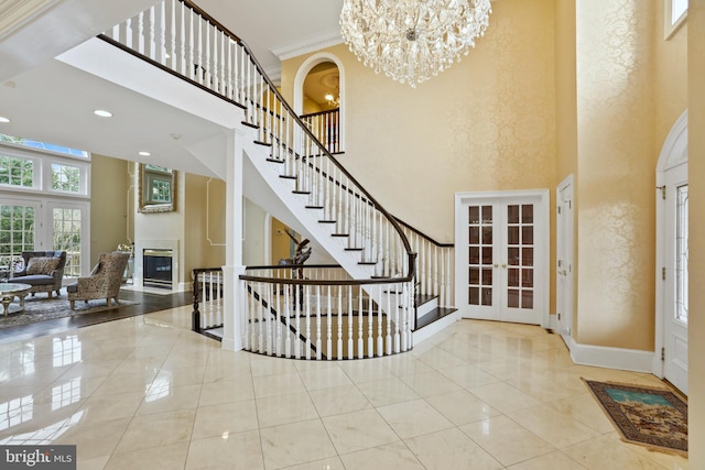 foyer with french doors, a notable chandelier, crown molding, a towering ceiling, and light tile patterned floors