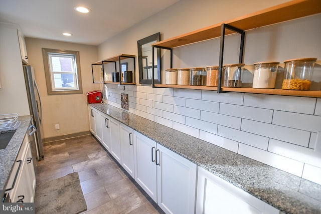 kitchen with decorative backsplash, stainless steel fridge, light stone counters, and white cabinetry