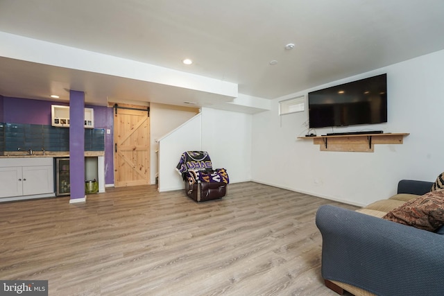 living room with a barn door, wet bar, beverage cooler, and light wood-type flooring