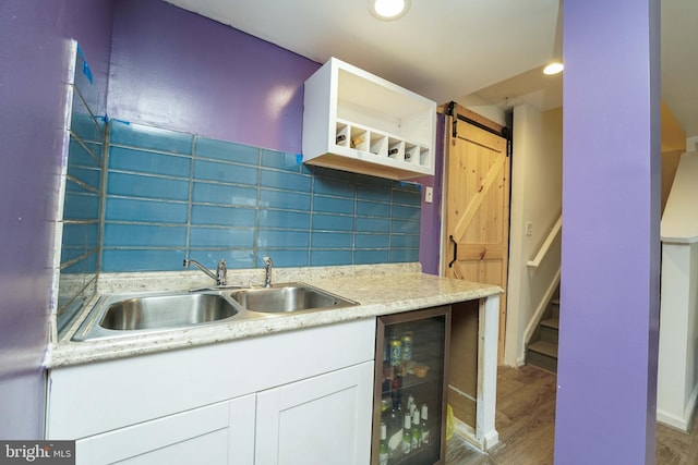 kitchen with sink, beverage cooler, a barn door, hardwood / wood-style floors, and white cabinets