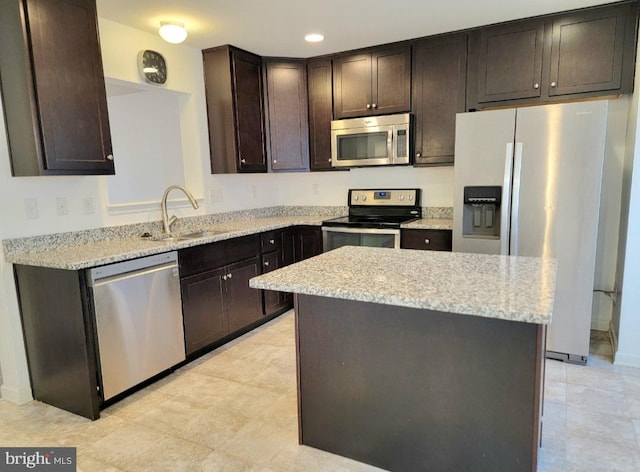 kitchen featuring light stone countertops, appliances with stainless steel finishes, dark brown cabinetry, sink, and a kitchen island