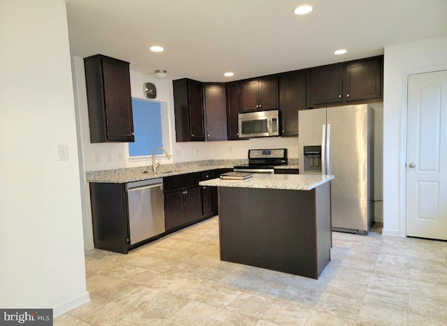 kitchen featuring sink, appliances with stainless steel finishes, dark brown cabinets, a kitchen island, and light stone counters