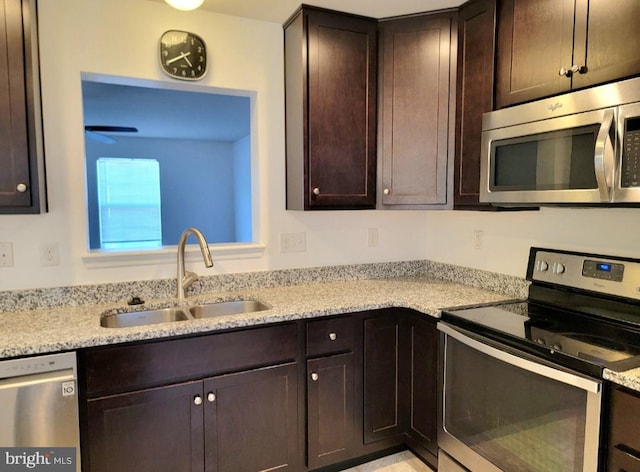 kitchen with dark brown cabinets, sink, light stone countertops, and stainless steel appliances