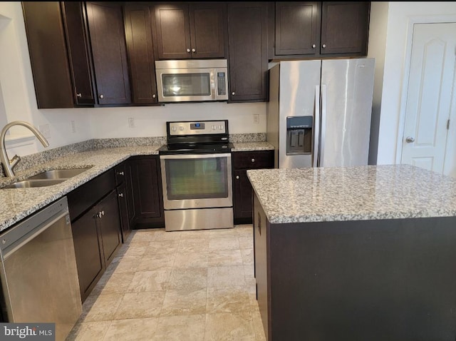 kitchen featuring appliances with stainless steel finishes, a center island, light stone counters, and sink