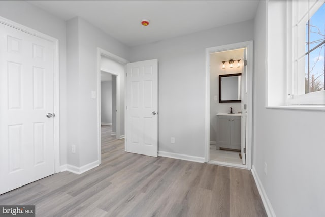 unfurnished bedroom featuring ensuite bathroom, sink, and light hardwood / wood-style flooring