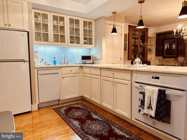 kitchen featuring tasteful backsplash, light hardwood / wood-style flooring, a chandelier, decorative light fixtures, and white appliances