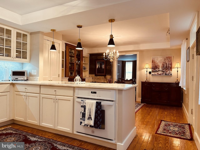 kitchen featuring hardwood / wood-style floors, an inviting chandelier, oven, decorative light fixtures, and kitchen peninsula