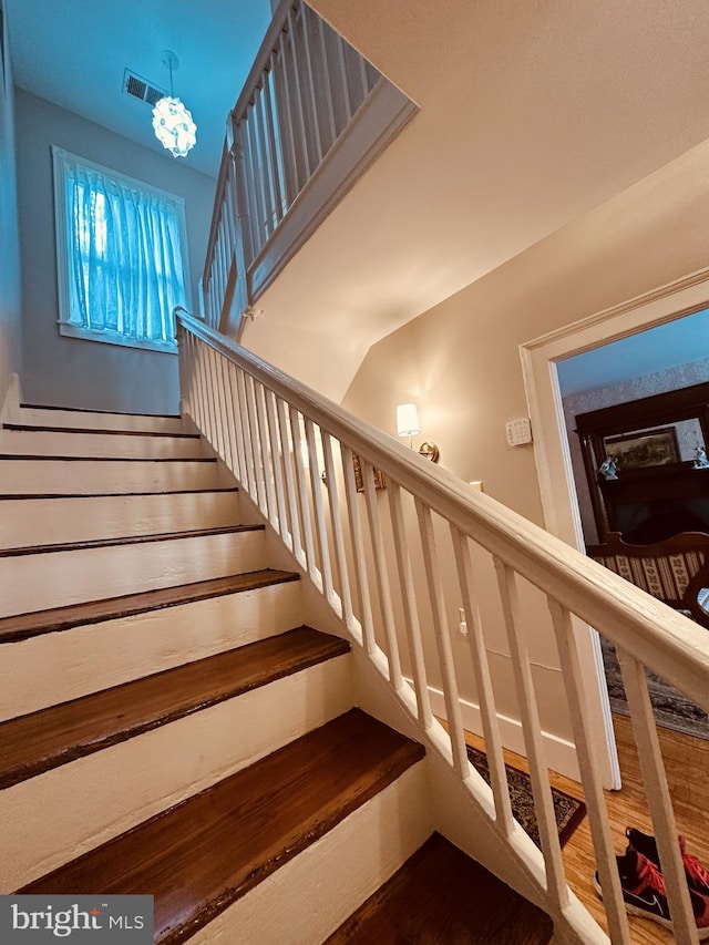 stairs with wood-type flooring, vaulted ceiling, and a notable chandelier