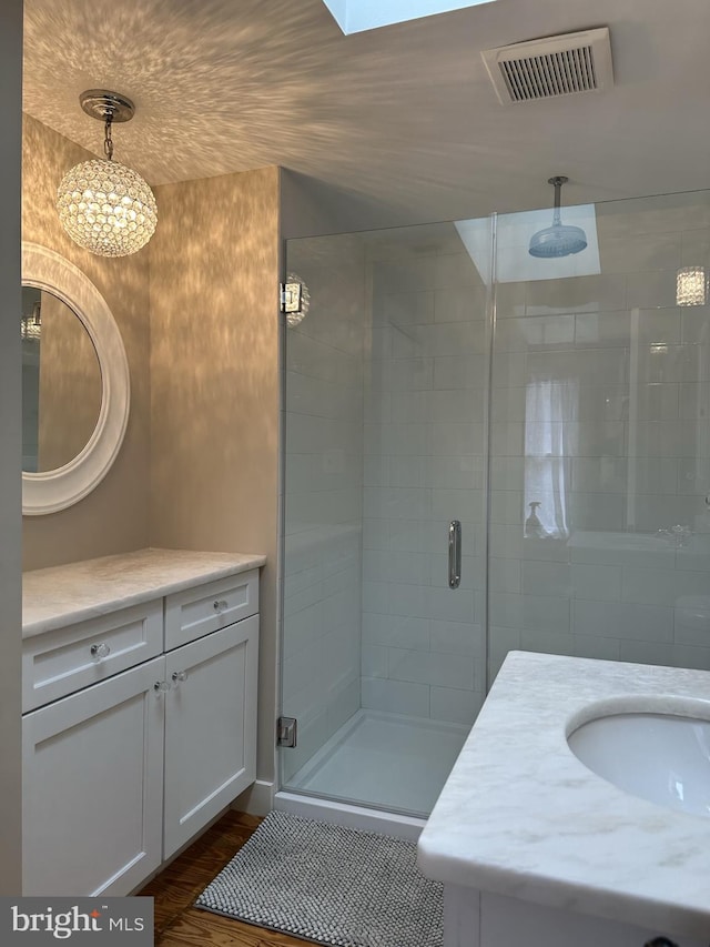 bathroom with wood-type flooring, vanity, a skylight, and walk in shower