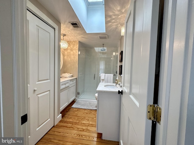 bathroom with hardwood / wood-style floors, vanity, a skylight, and a shower with shower door