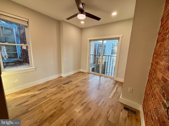 empty room featuring ceiling fan, light wood-type flooring, and brick wall