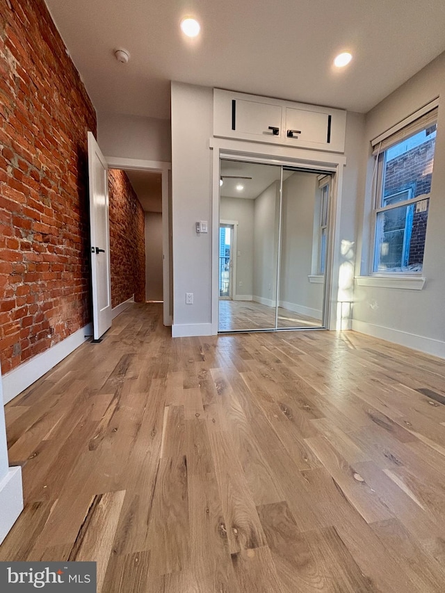 unfurnished bedroom with a closet, brick wall, and light hardwood / wood-style flooring