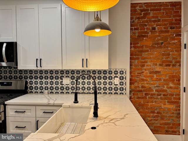 kitchen with light stone countertops, stove, white cabinetry, and brick wall