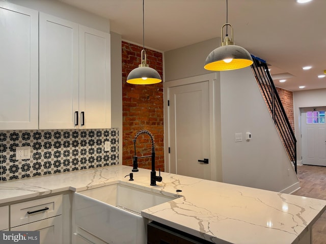 kitchen with light stone countertops, brick wall, sink, light hardwood / wood-style floors, and hanging light fixtures