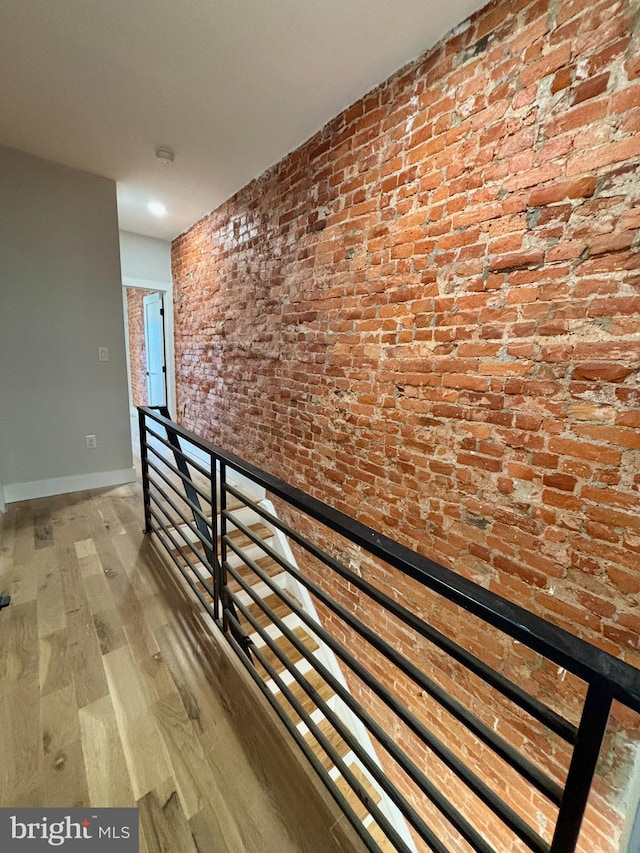 corridor with brick wall and hardwood / wood-style flooring