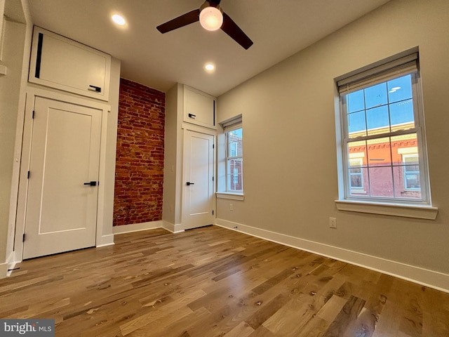 unfurnished bedroom featuring ceiling fan, light wood-type flooring, brick wall, and multiple windows