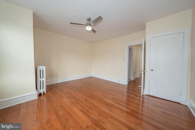 empty room with hardwood / wood-style flooring, radiator, and ceiling fan