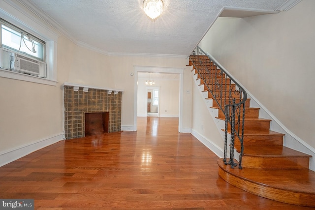 unfurnished living room featuring cooling unit, wood-type flooring, a textured ceiling, a fireplace, and ornamental molding