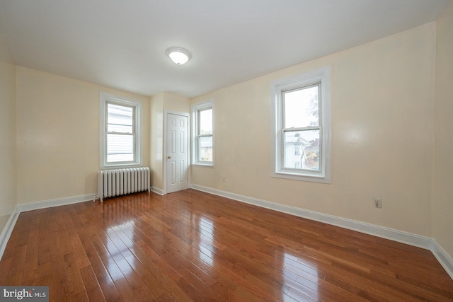 empty room with hardwood / wood-style flooring, plenty of natural light, and radiator