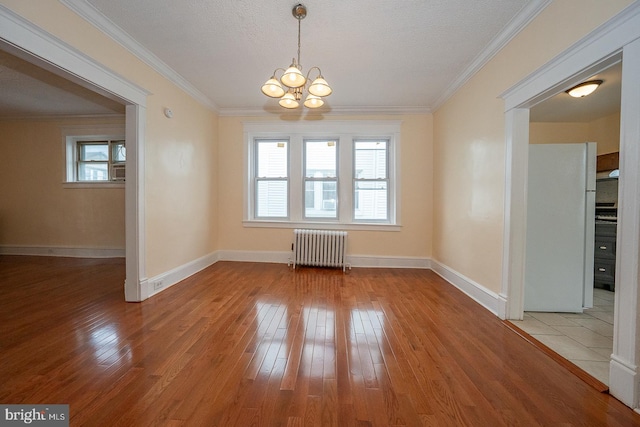 unfurnished dining area with hardwood / wood-style floors, a notable chandelier, a healthy amount of sunlight, and radiator heating unit