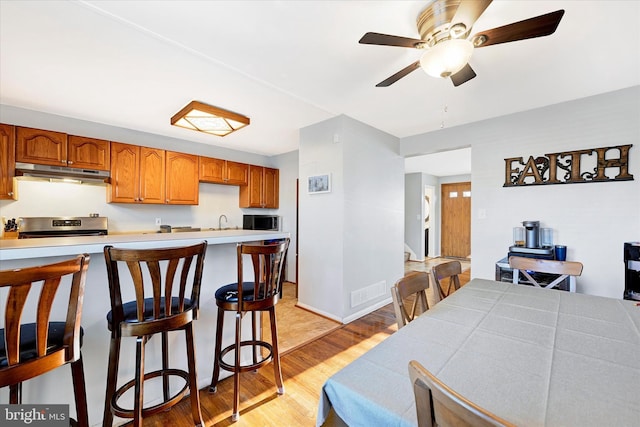 kitchen featuring ceiling fan, sink, light hardwood / wood-style floors, a breakfast bar area, and range