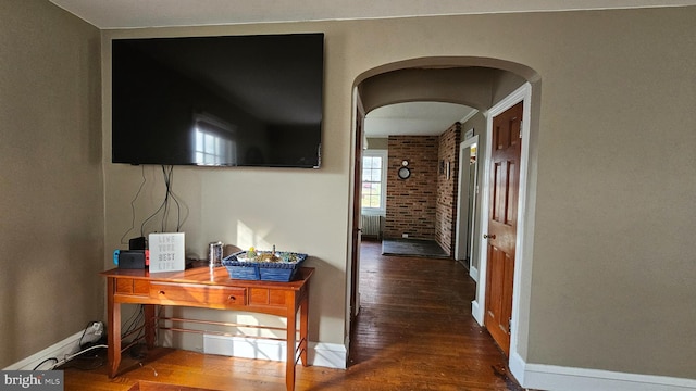 corridor with hardwood / wood-style floors and brick wall